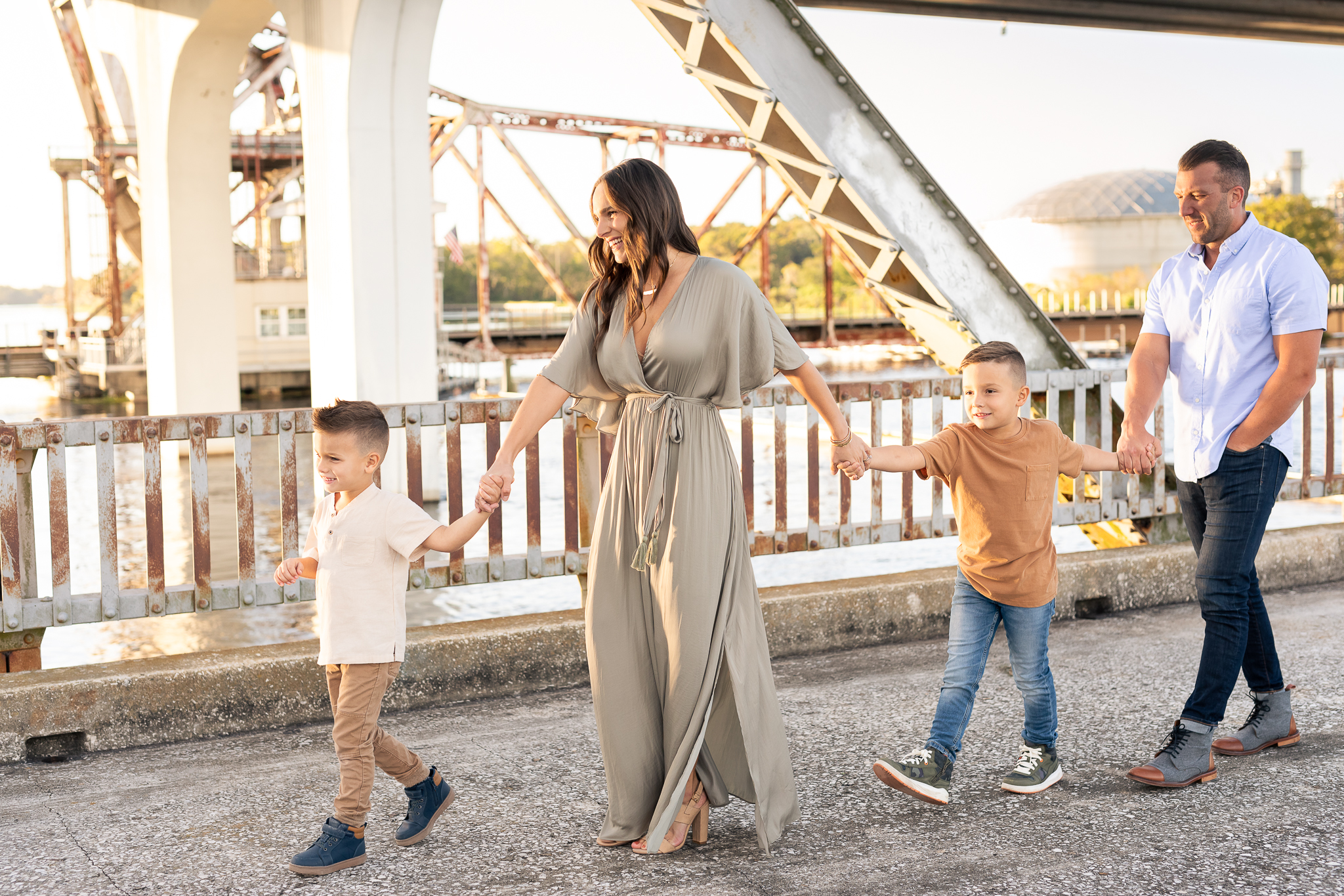 Family of four with two young children being prompt to walk holding hands and smiling at their fall family photo session in Lake Mary, Florida.