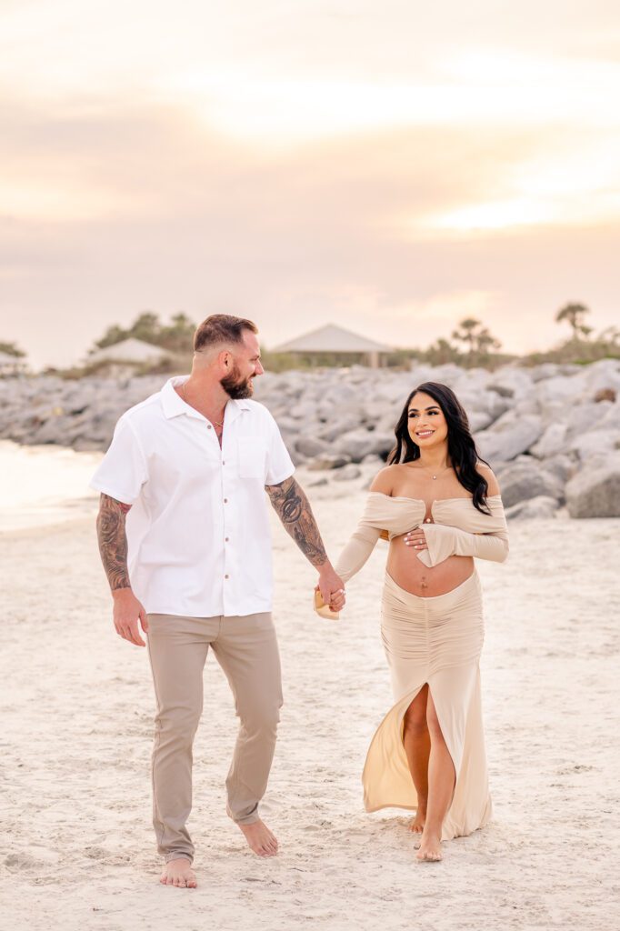 A couple walking looking at each other at the beach at their beach maternity photos in Orlando, Florida